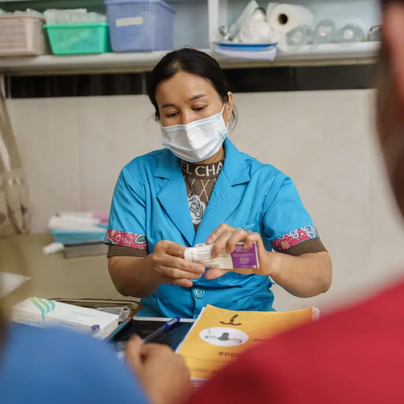 A woman wearing a blue shirt and face masks hands out medication.