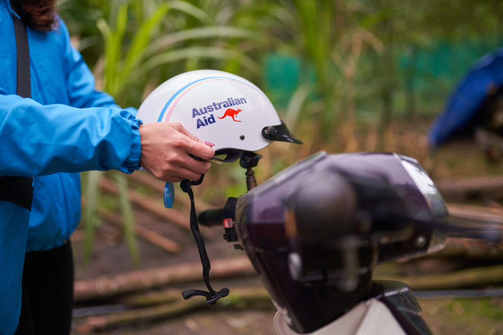 A person lifts a helmet labelled 'Australian Aid' from a motorcycle.