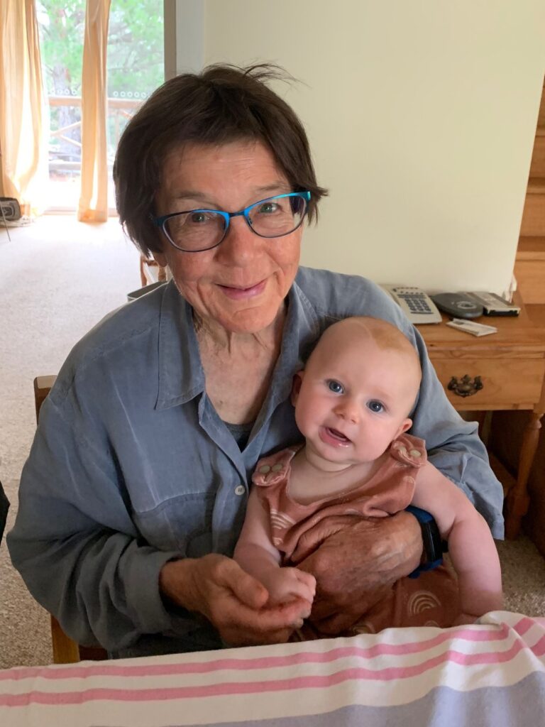 A woman with short brown hair sits at a table with a baby in her lap.