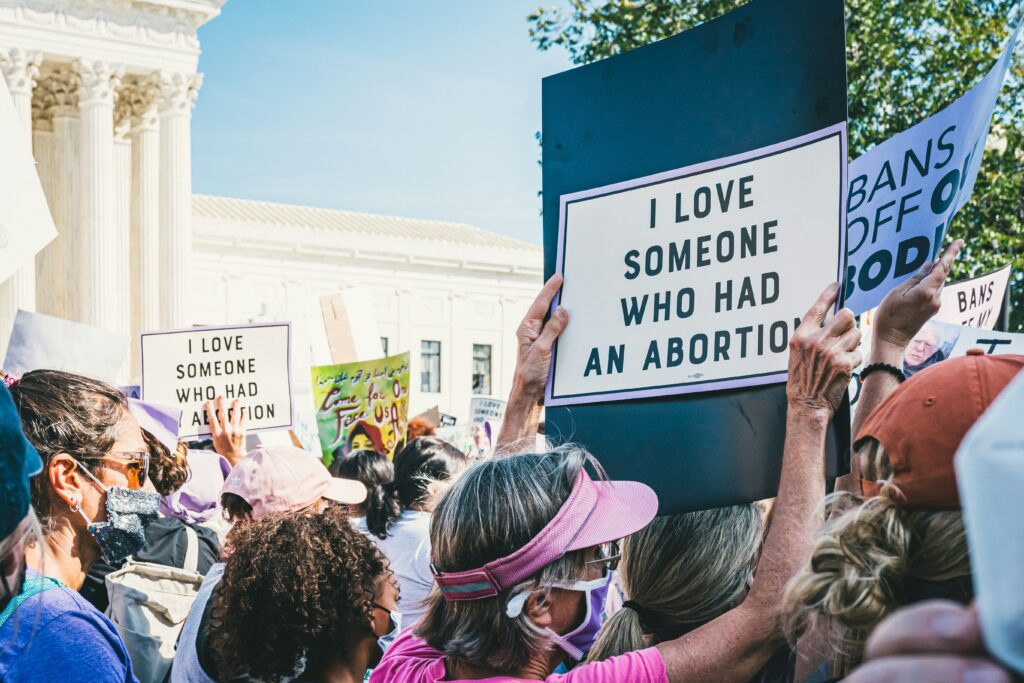 A group of protesters hold up pro-choice signs at a Washington DC rally. There is a white building with large columns in the background.