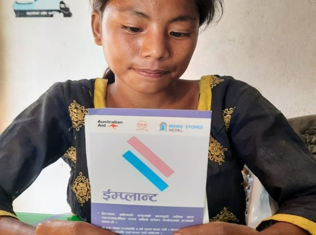 A young Nepali woman sits at a table and reads an information brochure.